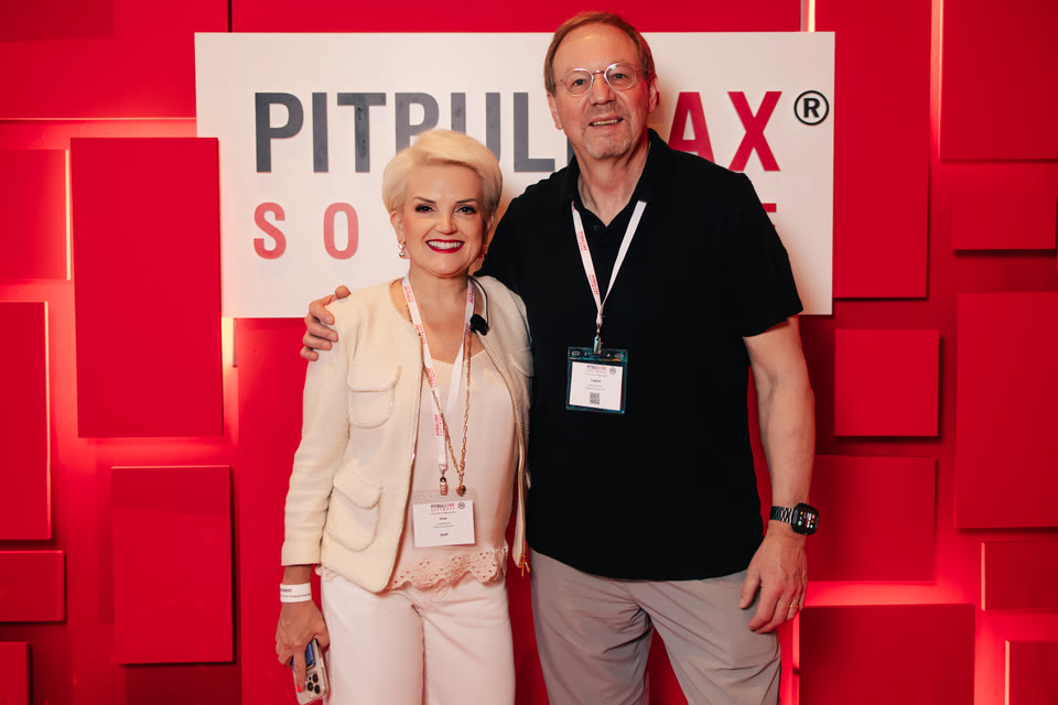 Two attendees posing in front of the PitBullTax® branded wall.