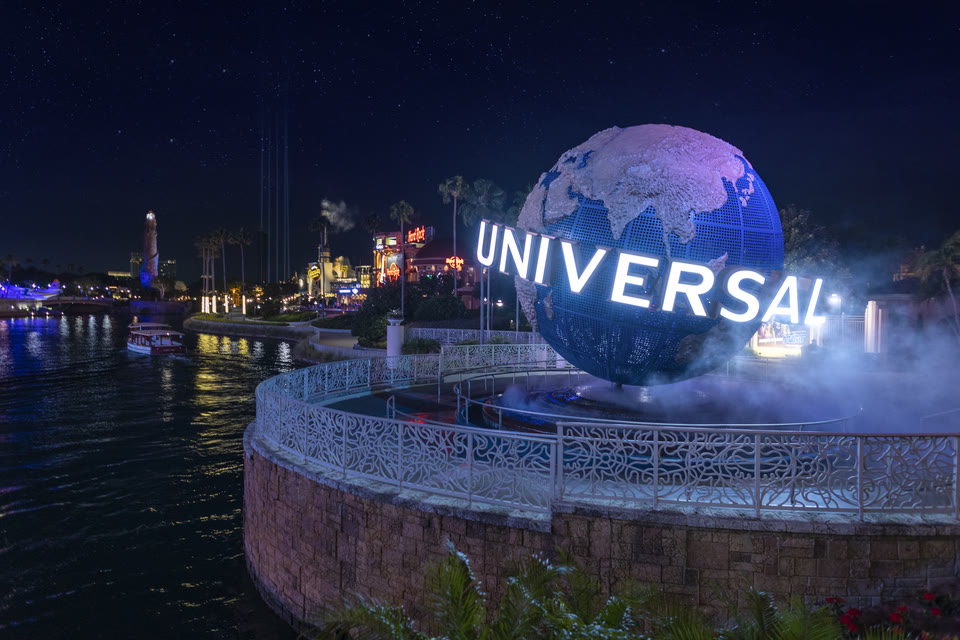 The illuminated Universal Orlando Resort globe at night with a water taxi passing on the lagoon.